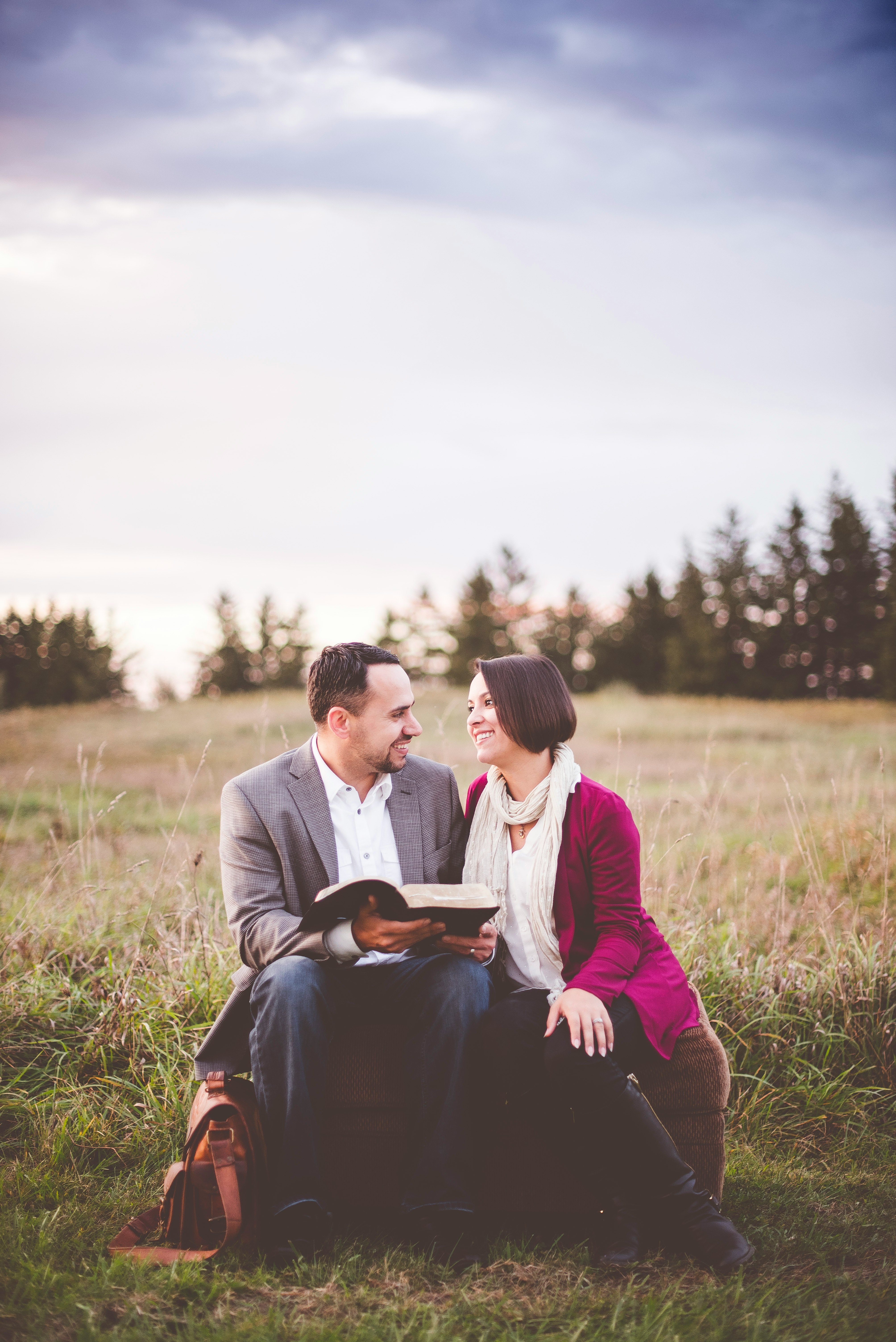 photo of man reading book to woman under grey cloudy sky